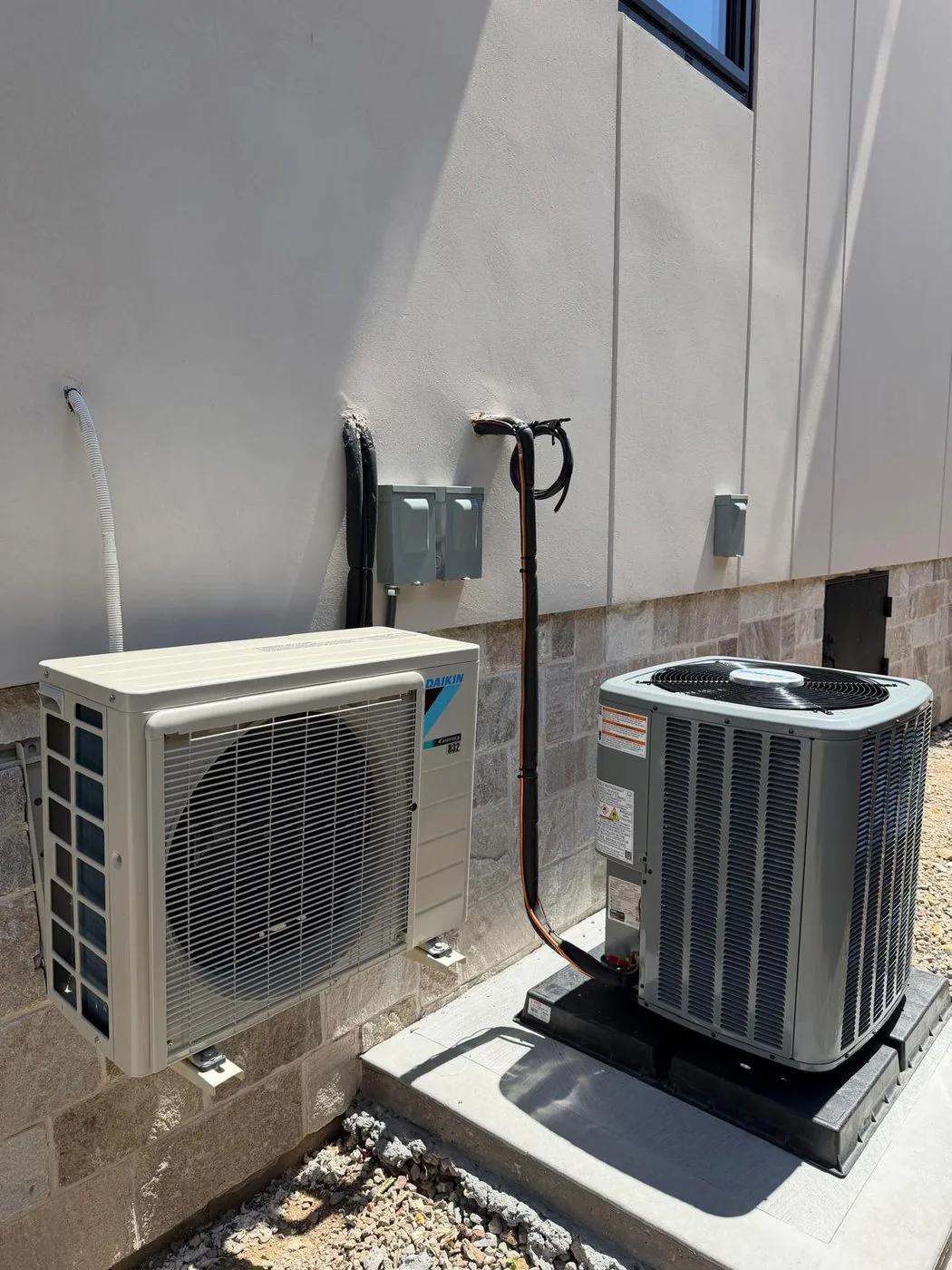 A newly installed ductless condenser and a central air condenser side by side on risers