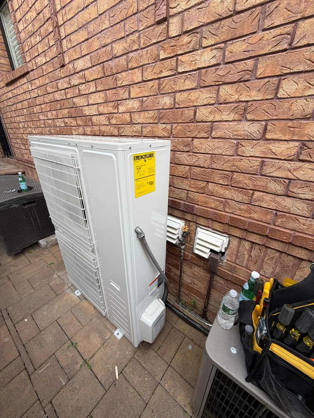 A ductless condenser mounted against a brick wall on a paver patio
