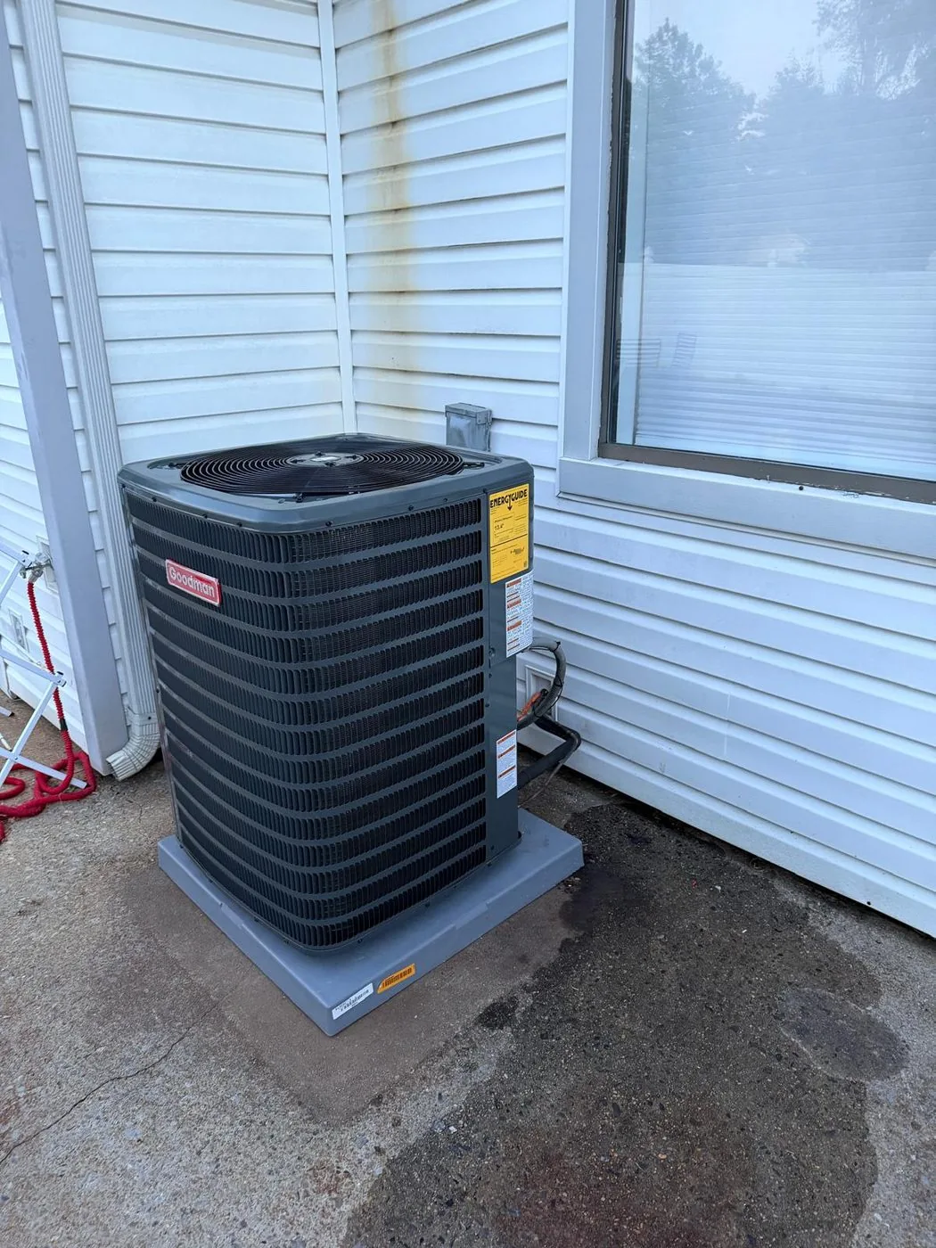 A replacement condenser installed on a level pad beside a window