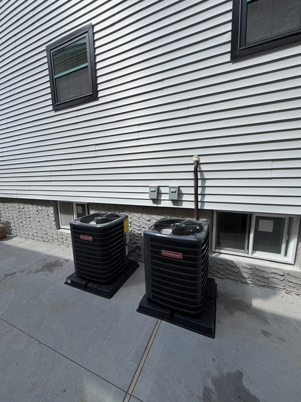 Two replacement condensers installed side by side on risers along a walkway